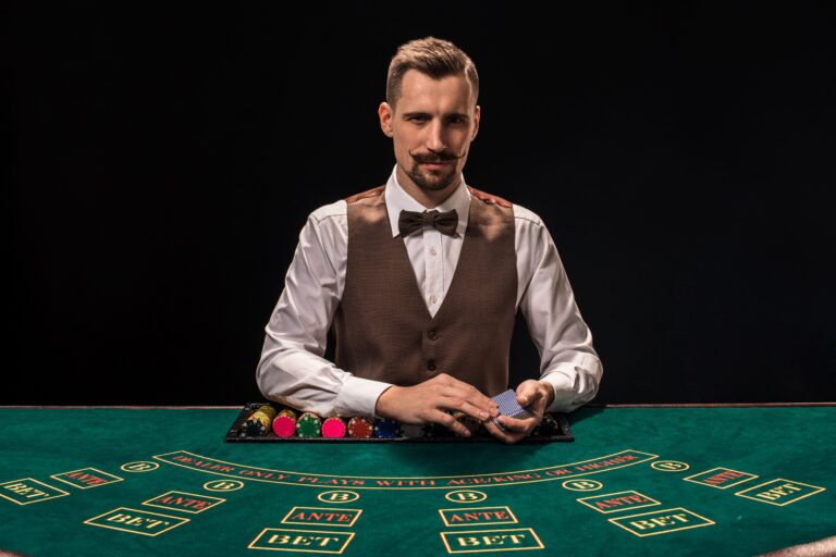 portrait-croupier-is-holding-playing-cards-gambling-chips-table-black-background-young-male-croupier-shirt-waistcoat-bow-tie-is-waiting-you-blackjack-table (1)